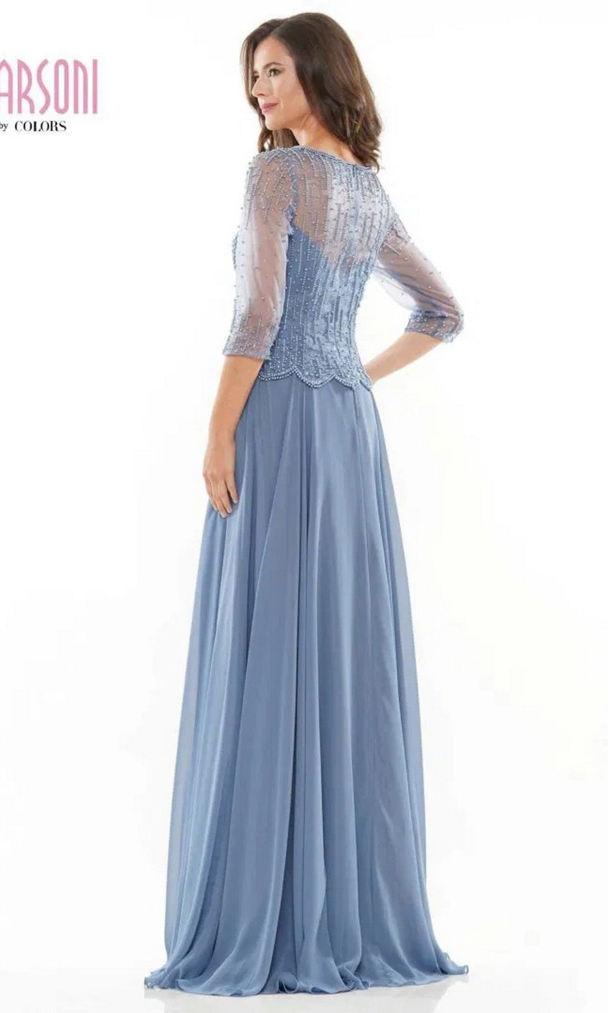 A woman stands facing sideways against a plain backdrop, wearing the Marsoni M312 long formal dress—a light blue gown with a beaded bodice, sheer embellished sleeves, and an elegant A-line skirt.